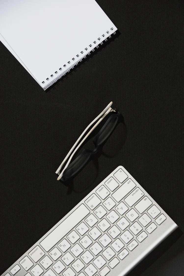 58dac37f-5a32-4133-9387-738f7e332a72-elevated-view-spiral-notepad-eyeglasses-keyboard-black-desk.jpg